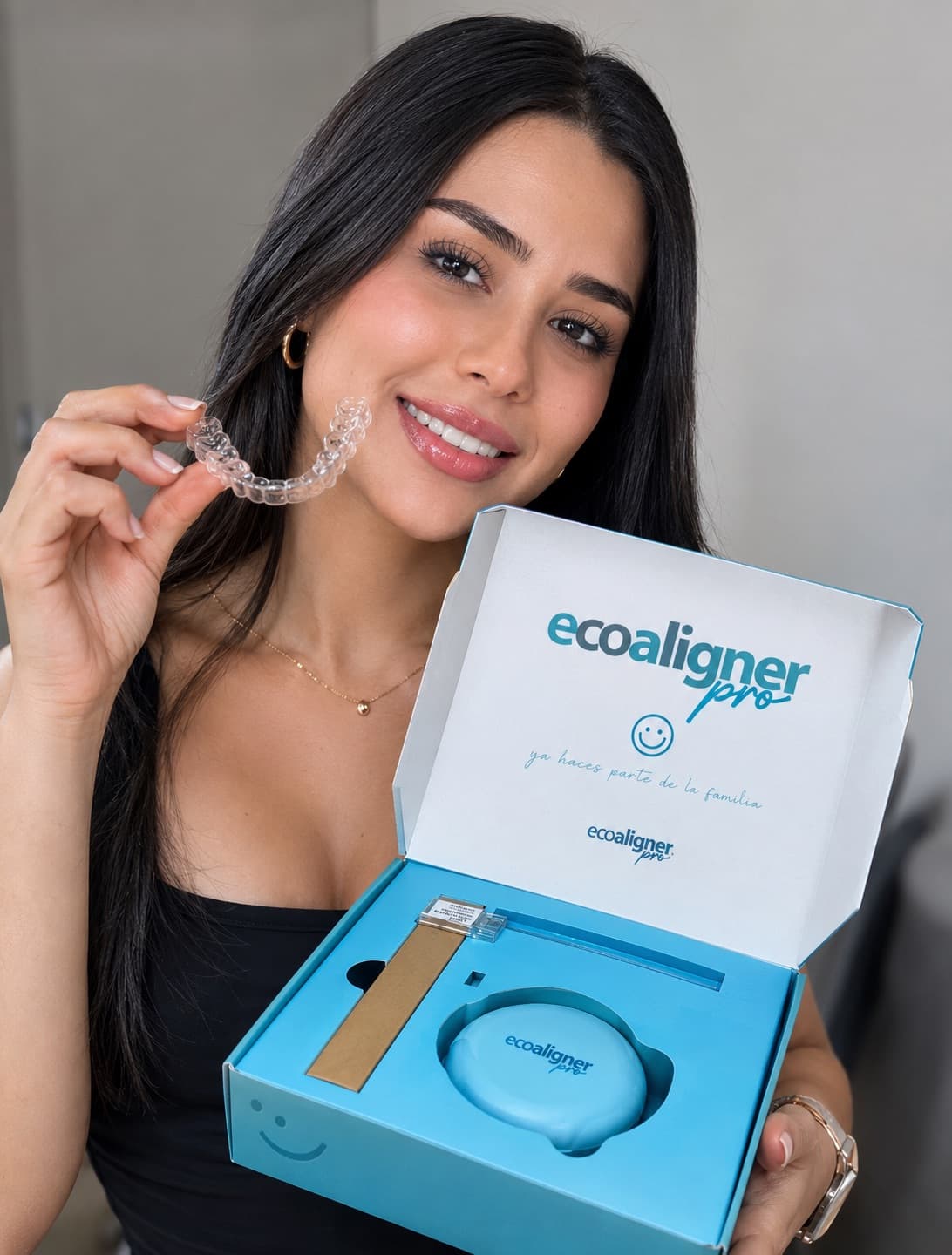 Una persona sostiene un alineador transparente junto al kit de EcoAligner Pro abierto, con el estuche y los accesorios dentro de la caja.
